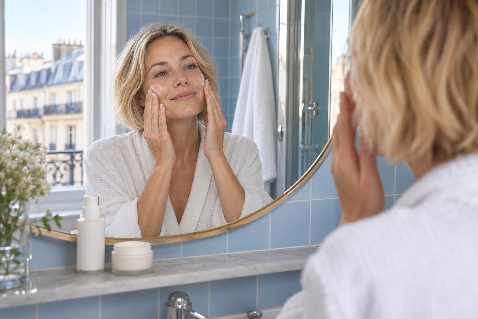 Femme blonde de plus de 40 ans appliquant une crème devant son miroir